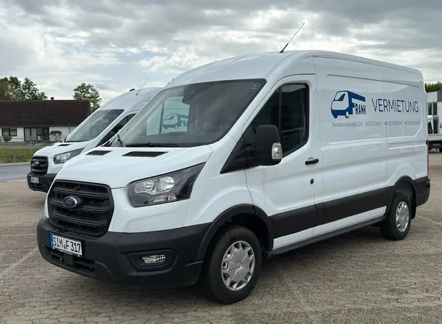 Weißer Ford Transit L2H2 mit der Beschriftung von Frank Vermietung, schräg von vorn, dahinter ein zweiter Transporter.